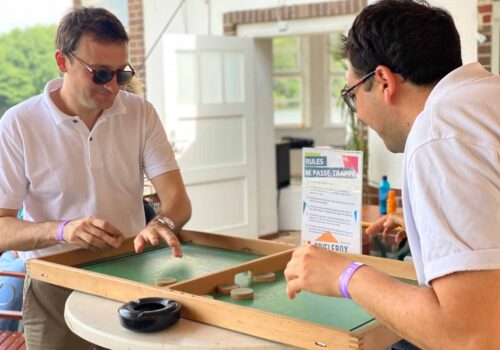 Zwei Männer mit Sonnenbrillen spielen ein Tischspiel names Le-Passe-Trappe.