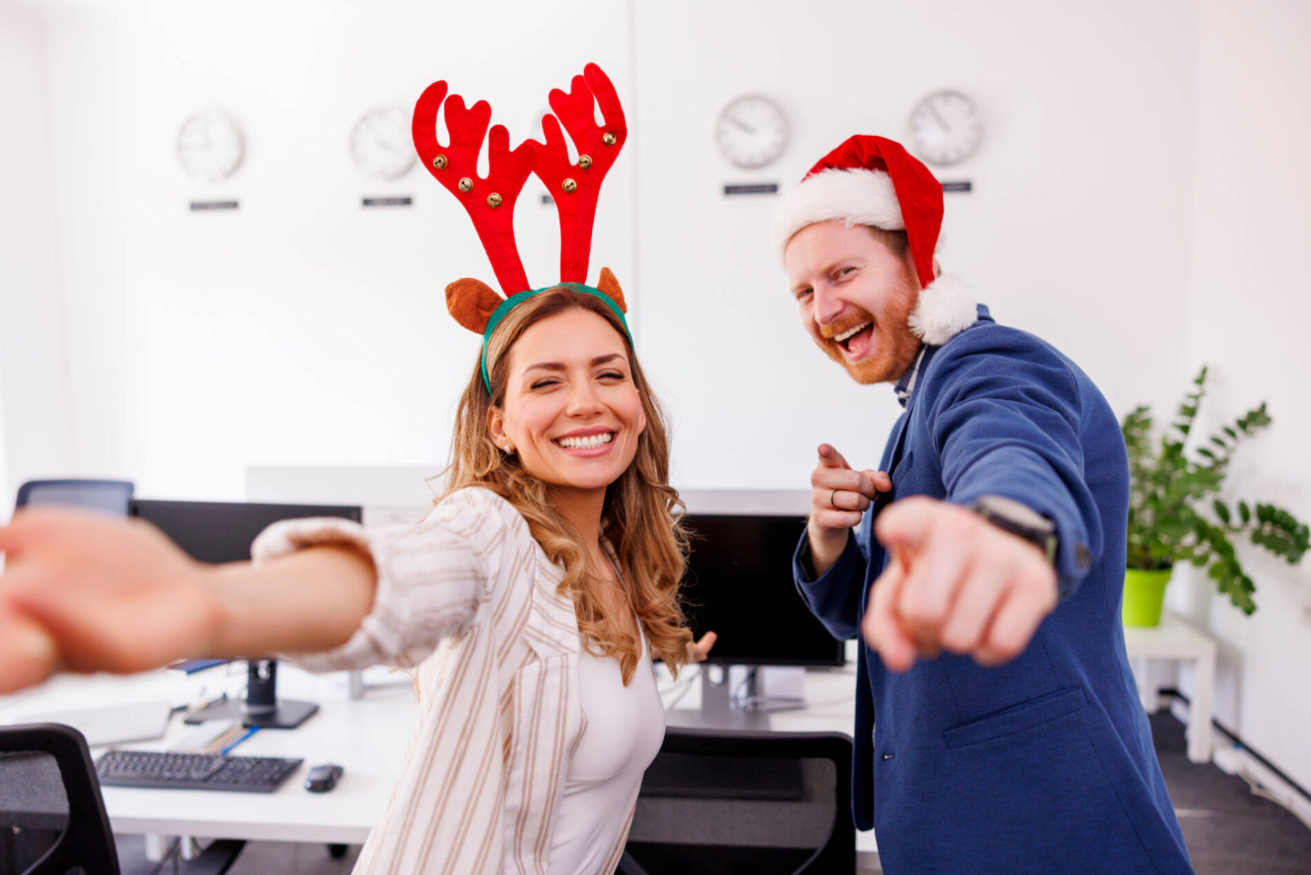 Fröhliche junge Geschäftsleute mit Weihnachtsmütze und Geweih haben Spaß beim Tanzen und Singen auf der Weihnachtsfeier im Büro.
