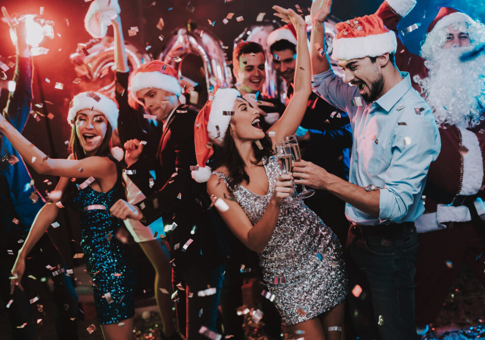 Glückliche junge Leute mit Weihnachtsmützen, die auf einer Weihnachtsparty tanzen, mit Weihnachtsmann.