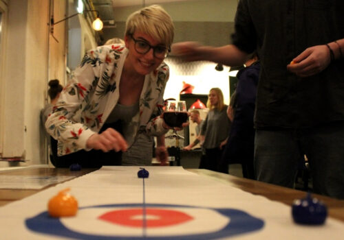 Eine blonde Frau spielt Mini-Curling auf einem Tisch.
